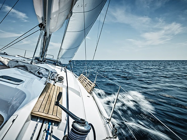 Eine Segelyacht fährt mit voller Fahrt über das blaue Wasser, während der Wind die Segel aufbläht und der Himmel in sanften Wolken verziert ist.