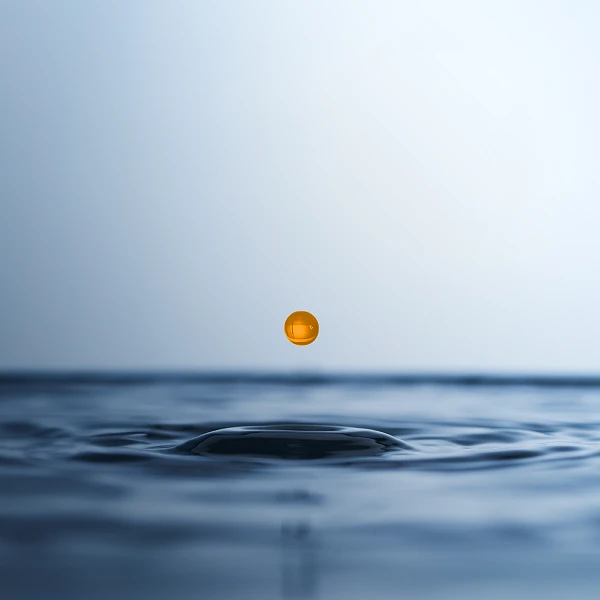 Eine orangefarbene Kapsel schwebt über der Wasseroberfläche und erzeugt konzentrische Wellenringe in einem sanften, blauen Hintergrund.