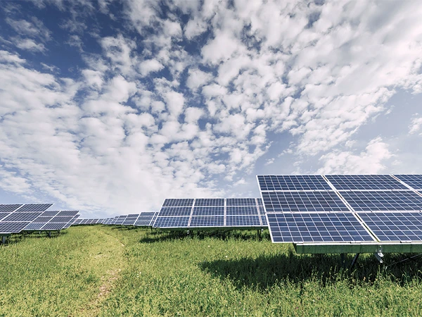 Ein Feld mit Solarpanels auf einer grünen Wiese unter einem blau-weißen, wolkigen Himmel.
