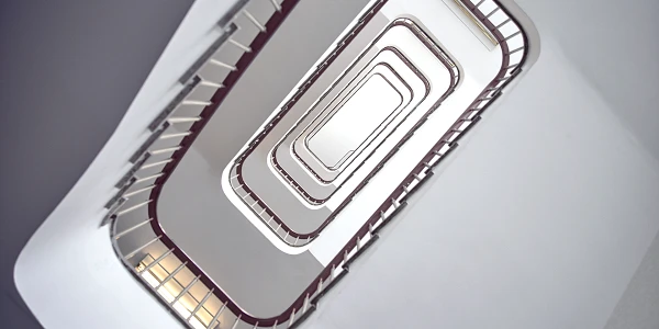 Eine spiralförmige Treppe ist von oben fotografiert, mit geschwungenen Geländern und einem minimalistischen, hellen Farbschema.
