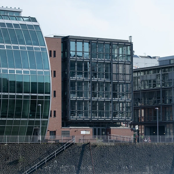Moderne Gebäude mit unterschiedlichen architektonischen Stilen, darunter große Glasfronten und gewellte Fassaden, stehen entlang eines Ufers.
