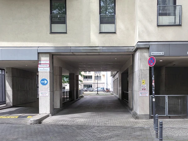 Ein Eingang zu einem Innenhof zwischen Gebäuden, jeweils mit verschiedenen Beschilderungen, darunter Verkehrs- und Parkhinweise.