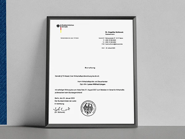Ein gerahmtes Dokument auf einem Tisch, das eine offizielle Mitteilung mit dem Bundesadler und dem Logo der Bundesregierung enthält. Das Dokument ist an Dr. Angelika Schmid adressiert und enthält Informationen zu einer Veranstaltung sowie ein Datum.