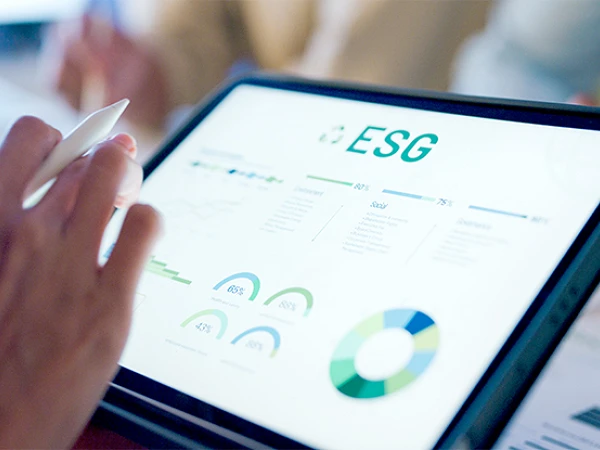 Eine Hand, die einen Stift hält, zeigt auf ein Tablet mit einer Grafik zu ESG-Daten, die verschiedene Diagramme und Statistiken präsentiert.