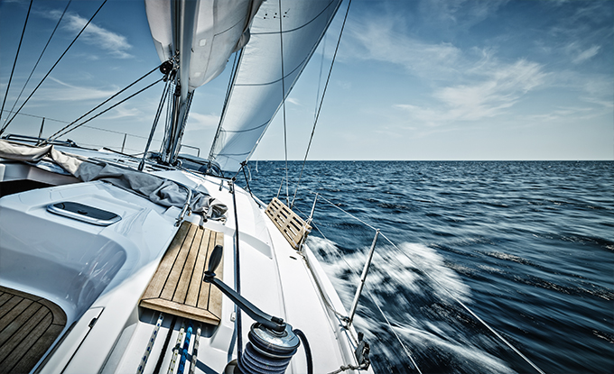 Eine Segelyacht fährt mit voller Fahrt über das blaue Wasser, während der Wind die Segel aufbläht und der Himmel in sanften Wolken verziert ist.