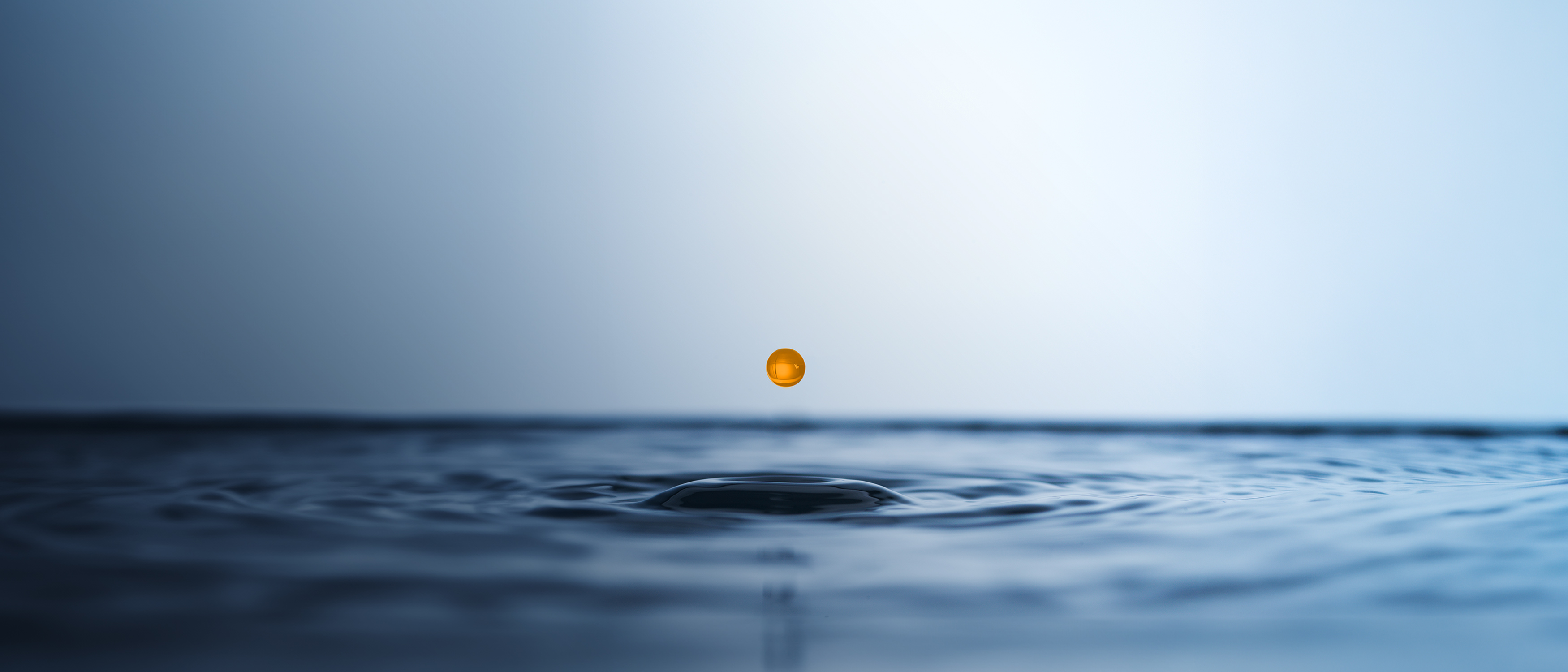 Eine orangefarbene Kapsel schwebt über der Wasseroberfläche und erzeugt konzentrische Wellenringe in einem sanften, blauen Hintergrund.