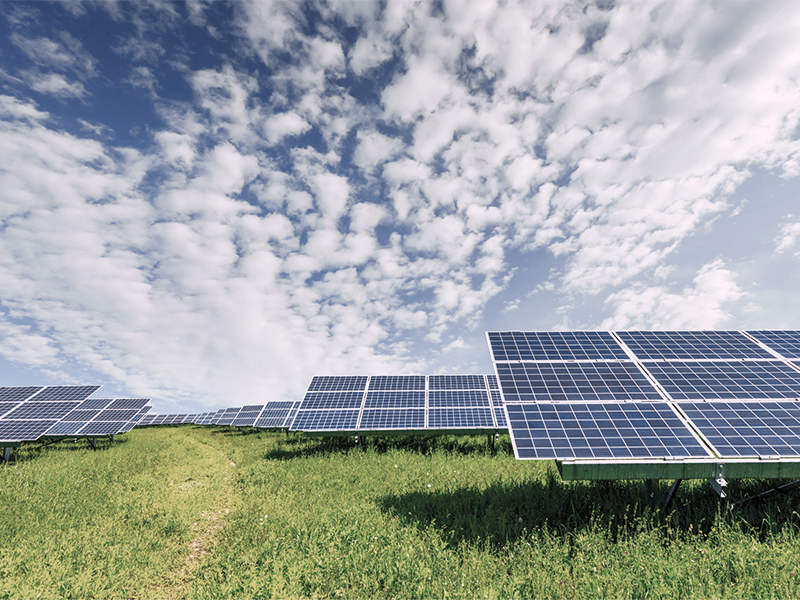 Ein Feld mit Solarpanels auf einer grünen Wiese unter einem blau-weißen, wolkigen Himmel.