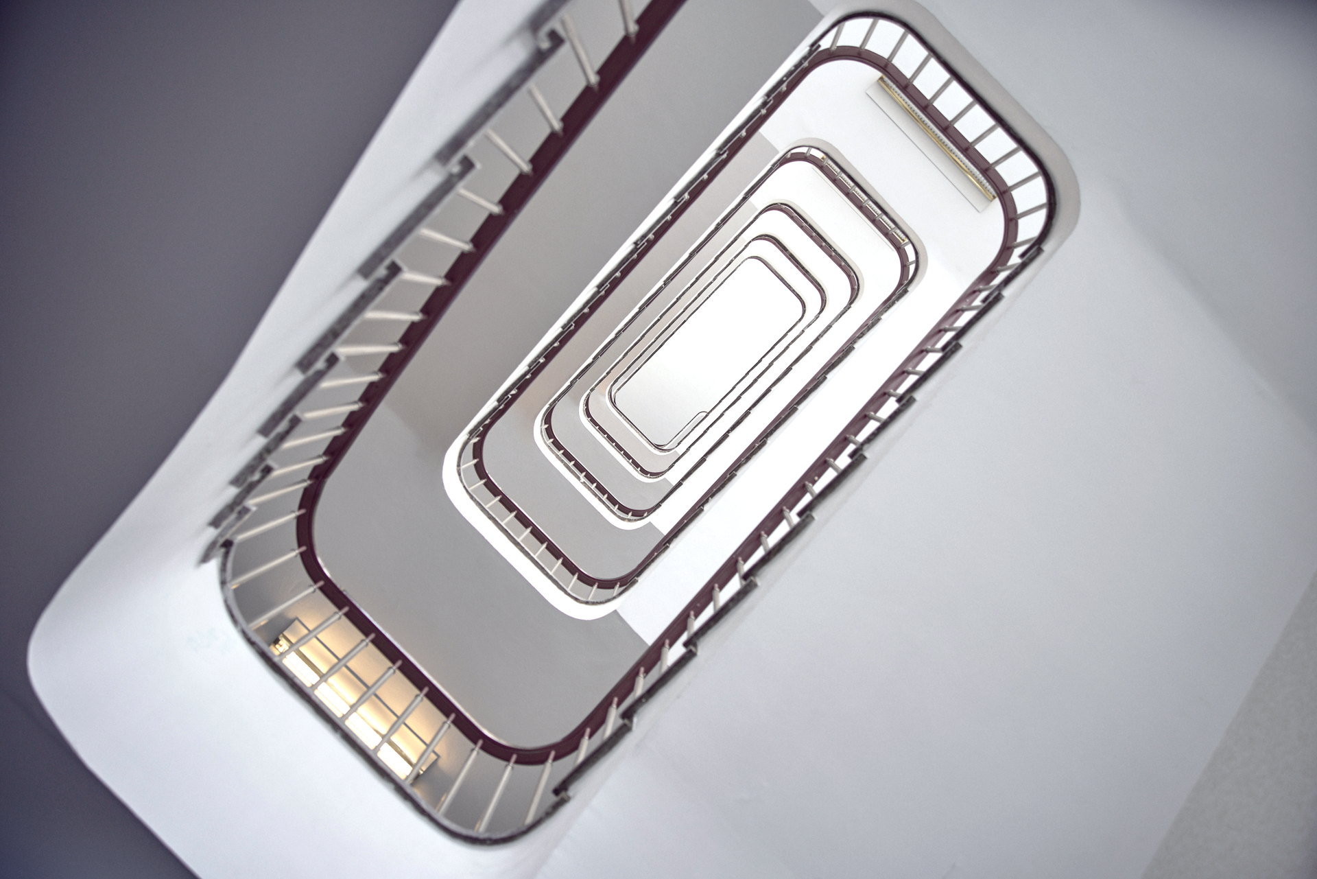 Eine spiralförmige Treppe ist von oben fotografiert, mit geschwungenen Geländern und einem minimalistischen, hellen Farbschema.