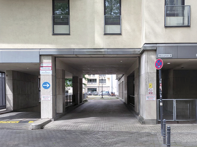 Ein Eingang zu einem Innenhof zwischen Gebäuden, jeweils mit verschiedenen Beschilderungen, darunter Verkehrs- und Parkhinweise.