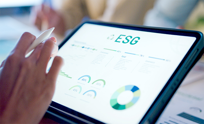 Eine Hand, die einen Stift hält, zeigt auf ein Tablet mit einer Grafik zu ESG-Daten, die verschiedene Diagramme und Statistiken präsentiert.